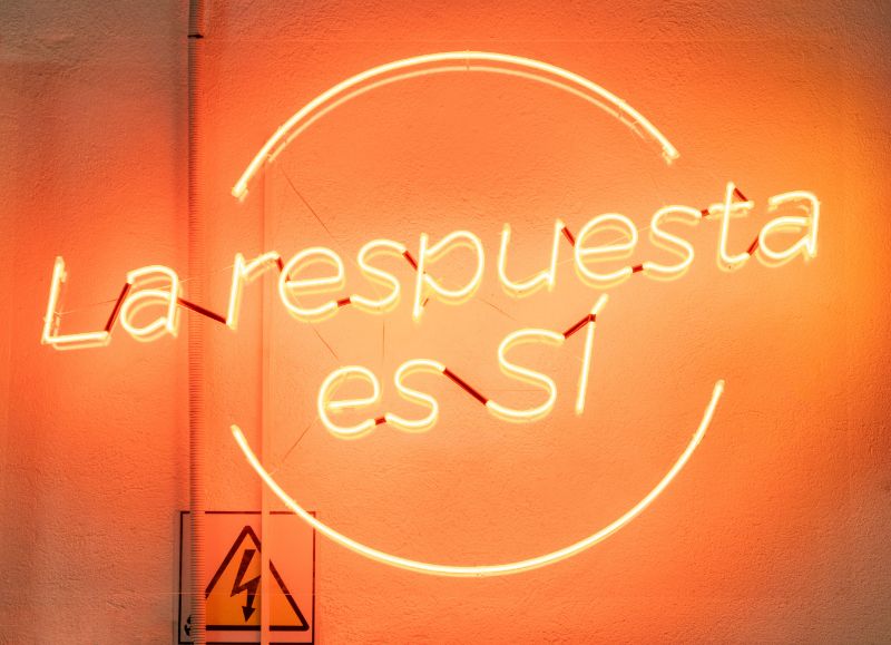 Frase La respuesta es Sí y dos trazos luminosos sobre una pared naranja