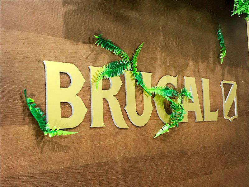 Letras Brugal de color dorado y vegetación sobre una pared marrón